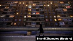 Женщина идет на фоне панельного жилого дома советской постройки. 