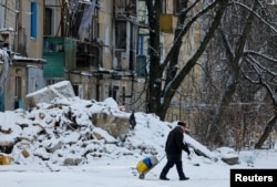 Un bărbat trage un cărucior lângă o clădire avariată din Avdiivka, o regiune ucraineană trecută sub control rusesc - 16 februarie 2025