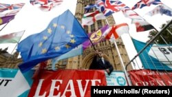 Un protestatar anti-Brexit, fluturând un steag al UE, alături de o pancardă pro-Brexit. Imagine de la finalul lunii octombrie, în fața Palatului Westminster