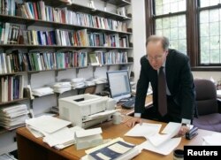 Një profesor shihet duke analizuar letrat që ka në tavolinë.