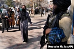 Afghan women pass by a Taliban fighter on a street in Kabul.