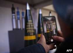 Мужчина фотографирует 155-мм боеприпасы на месте будущего артиллерийского завода, где немецкий производитель оружия Rheinmetall планирует начать производство с 2025 года, в Унтерлюссе, Германия, 12 февраля 2024 года