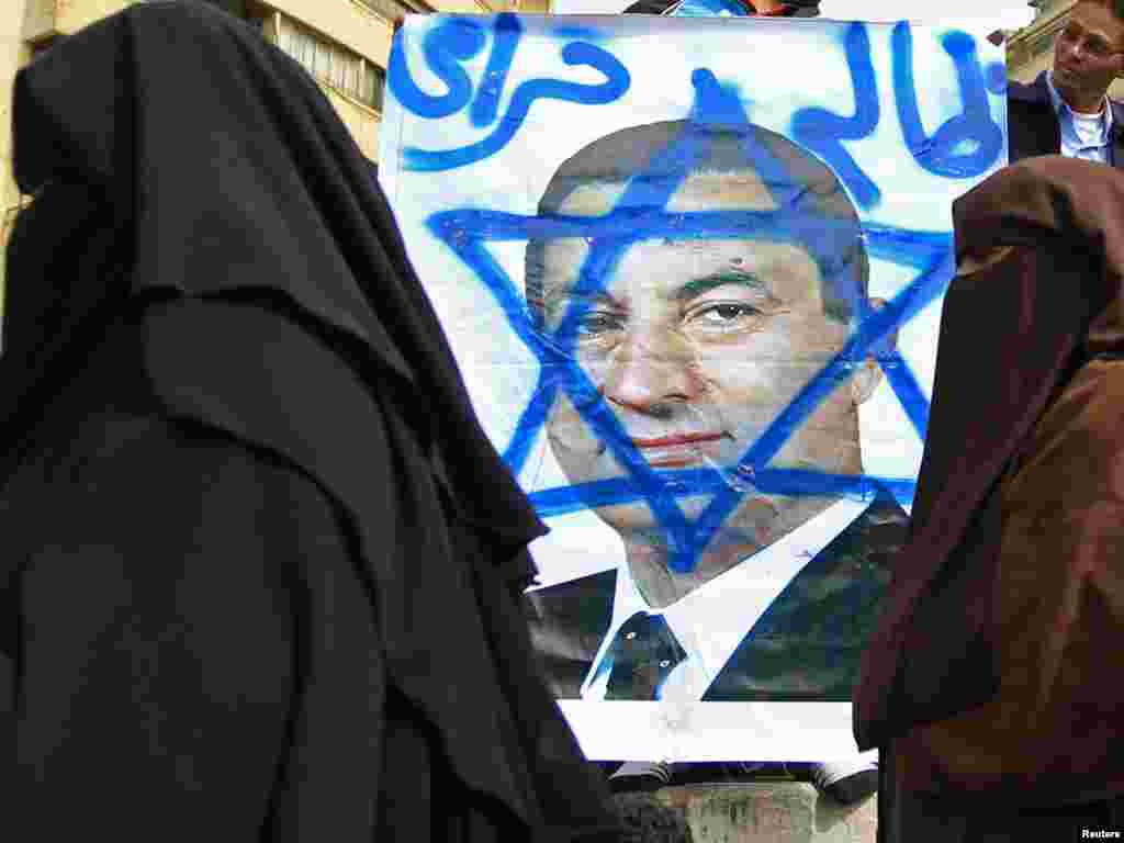 Women walk past an opposition supporter holding a poster of Mubarak painted with the Star of David.