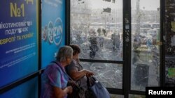 Femei așteptând într-o stație de autobuz avariată de lovituri aeriene rusești la Kiev, pe 10 iulie 2025.