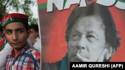 supporters of Pakistan's cricketer-turned politician and head of the Pakistan Tehreek-e-Insaf (Movement for Justice) party Imran Khan stands next to poster with a picture of Khan as they gather near his residence in Islamabad on July 26.
