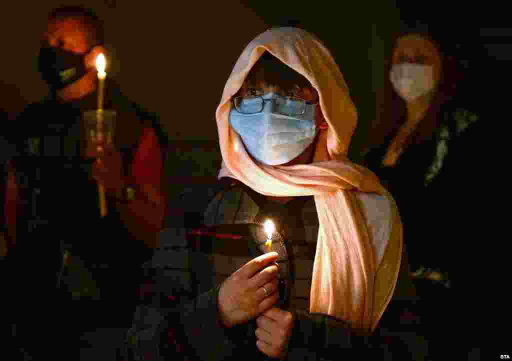 Болгарська православна християнка у захисній масці тримає свічку під час вечірнього пасхального богослужіння у Церкві св. Кирила та Мефодія в Іспериху, Болгарія