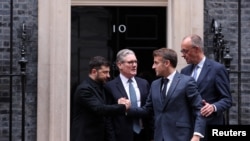 Presidenti ukrainas Volodymyr Zelensky (majtas) ia zgjat dorën presidentit francez Emmanuel Macron para 10 Downing Street, pas një takimi në Londër, ku morën pjesë edhe kryeministri britanik, Keir Starmer (i dyti majtas) e kancelari gjerman, Friedrich Merz (djathtas), 8 dhjetor.