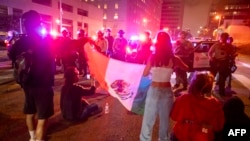 Protestatarii cu un steag mexican se confruntă cu forțele de ordine pe străzile din jurul clădirilor federale din Los Angeles, California. 8 iunie 2025