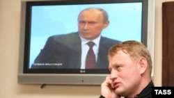 Former police Major Aleksei Dymovsky walks past a video screen showing Prime Minister Vladimir Putin.