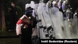 Протестующий с грузинским флагом разговаривает с сотрудниками полиции, которые блокируют улицу во время митинга оппозиции в день местных выборов в Тбилиси. Грузия, 4 октября 2025 года