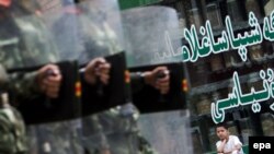 Мальчик-уйгур сидит возле магазина, наблюдая, как китайские солдаты идут по улице Урумчи, 12 июля 2009 года.  