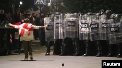 A protester wearing a Georgian flag walks toward police officers blocking the street during an opposition rally on the day of Georgian local elections in Tbilisi on October 4. 