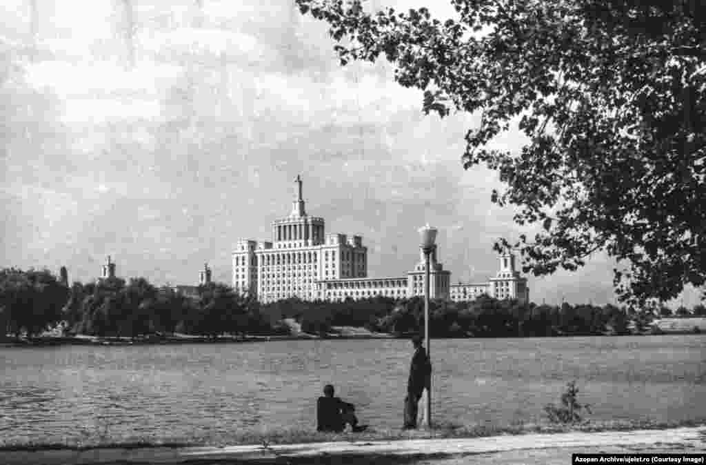 Bărbații privesc peste Lacul Herăstrău din București spre Casa Scânteii, construită de sovietici după modelul Universității Lomonosov de la Moscova. Szocs este unul dintre fondatorii Azopan, o arhivă fotografică cu acces liber care conține fotografii făcute mai ales de reporteri amatori din secolul al XX-lea din România, ceea ce înseamnă că infrastructura necesară pentru arhiva Uj Elet era deja în mare parte existentă.