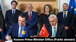 Kryeministri i Kosovës, Albin Kurti, i pari majtas, duke nënshkruan marrëveshjen për fabrikën e municioneve.