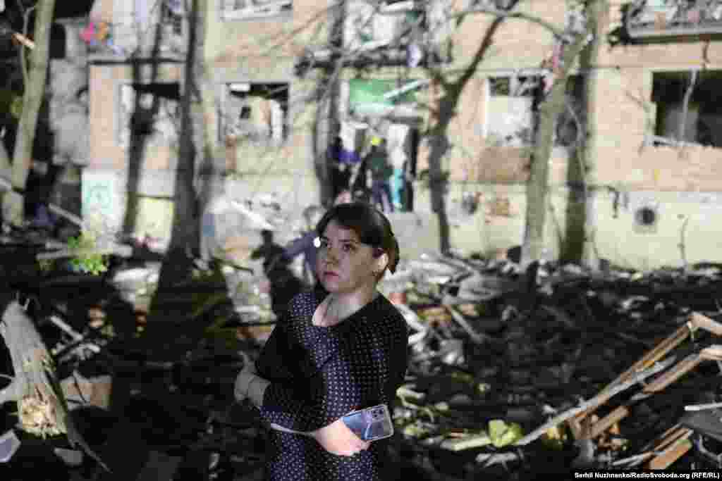 A woman stands outside a damaged apartment building in Kyiv.