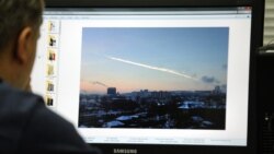 A man in Moscow looks at a computer screen displaying a picture reportedly taken in the Urals city of Chelyabinsk, showing the trail of a falling object above a residential area of the city.