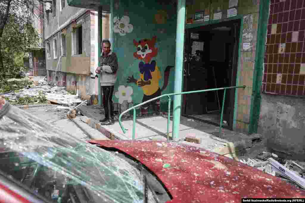 Чоловік стоїть біля свого підʼїзду в багатоквартирному будинку, який постраждав під час обстрілу, позаду нього намальований Кіт Леопольд – один із героїв радянських мультфільмів