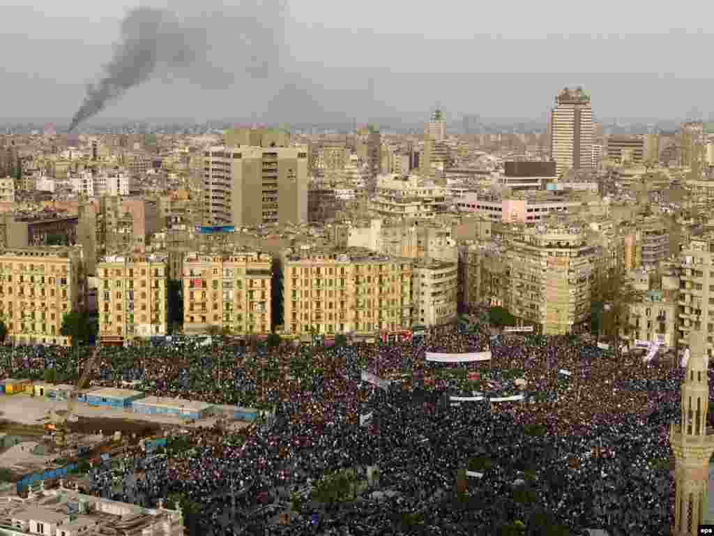 Smoke rises from an unknown location as protesters rally in Tahrir Square.