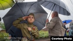 Un copil în uniformă sovietică și cu panglica „Sfântul Gheorghe” la piept dă salutul militar la manifestația de 9 mai de la Tiraspol.
