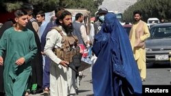 Forțele talibane blochează drumurile din jurul aeroportului, în timp ce o femeie îmbrăcată în Burqa trece pe lângă, Kabul, Afganistan. Fotografie realizată în 27 august 2021.