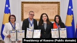 Tre të mbijetuarit e dhunës seksuale gjatë luftës në Kosovë, Shyrete Tahirit (e para majtas), Ramadan Nishori pranë presidentes Vjosa Osmani dhe Vasfije Krasniqit (e para djathtas), pranojnë medalje nderi, 18 prill, Prishtinë.
